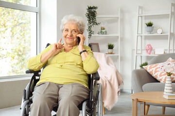Senior woman in wheelchair talking by mobile phone at home