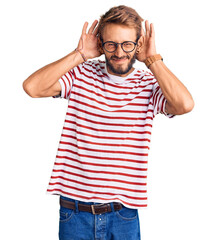 Handsome blond man with beard wearing casual clothes and glasses trying to hear both hands on ear gesture, curious for gossip. hearing problem, deaf