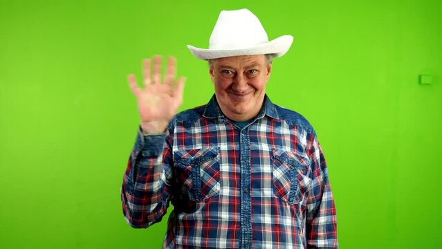 Senior man in white cowboy hat waves palm for greeting or goodbye sign.