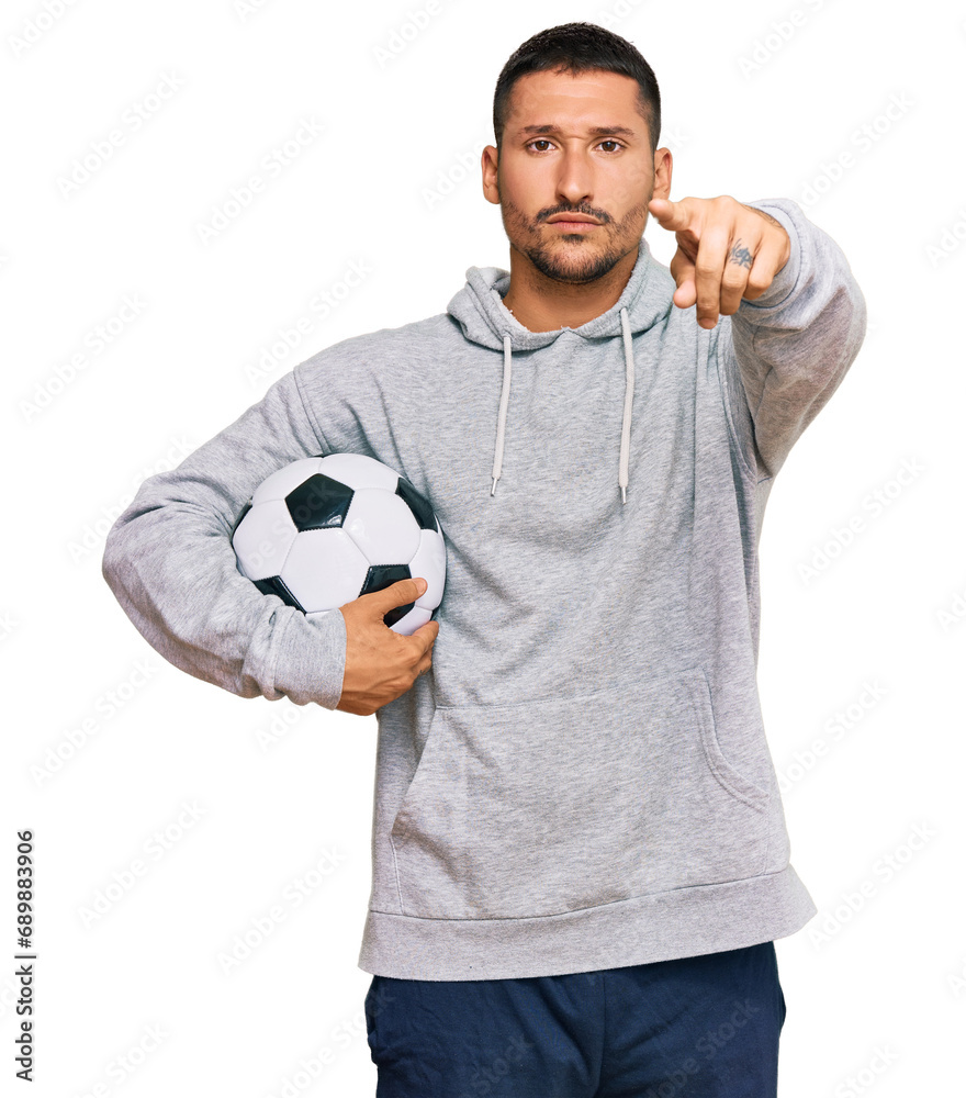 Poster Handsome man with tattoos holding soccer ball pointing with finger to the camera and to you, confident gesture looking serious