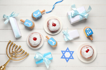Hanukkah composition with donuts, dreidels, menorah and gift boxes on white wooden background