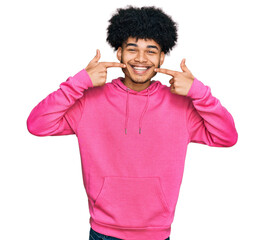 Young african american man with afro hair wearing casual pink sweatshirt smiling cheerful showing and pointing with fingers teeth and mouth. dental health concept.