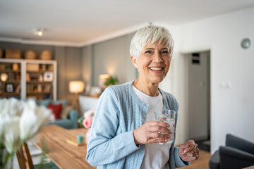 An elderly woman drinks water from a glass, she is in her apartment in the living room, dehydration