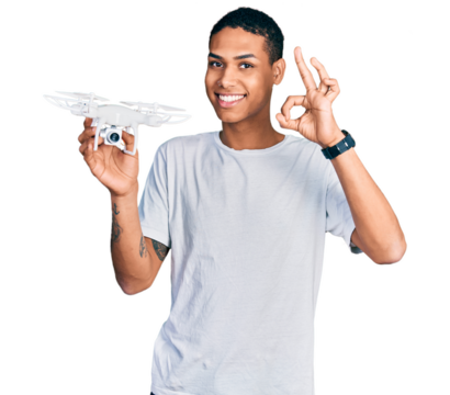 Young hispanic man holding drone doing ok sign with fingers, smiling friendly gesturing excellent symbol