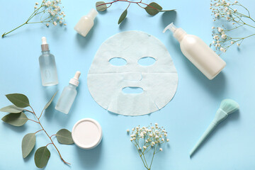 Facial sheet mask with different cosmetic products and gypsophila flowers on blue background