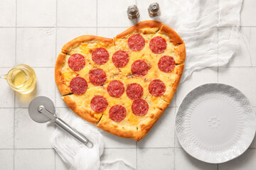 Tasty heart shaped pizza with oil and cutter on white tile background