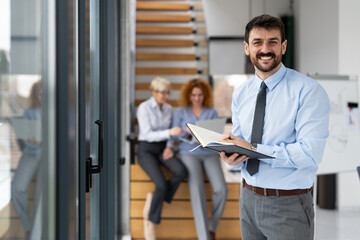 Naklejka na ściany i meble Smiling businessman holding notebook at office