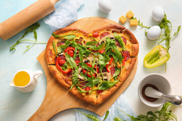 Wooden board with tasty heart shaped pizza and ingredients on light blue background