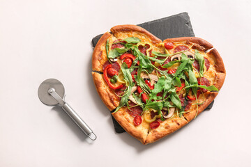 Board with tasty heart shaped pizza and cutter on white background