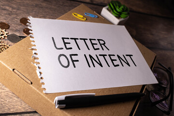 LETTER OF INTENT text on a paper clipboard with magnifier and keyboard on wooden background