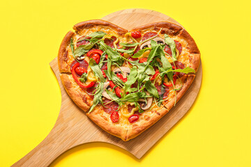 Wooden board with tasty heart shaped pizza on yellow background