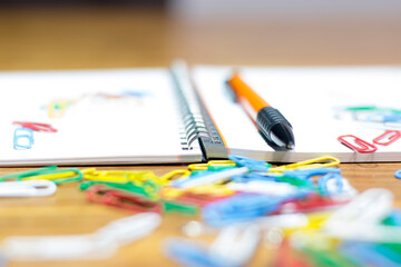 Close up view of colored paperclips notepad and pencil. Messy table