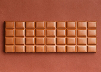 Large chocolate bar on brown background, top view