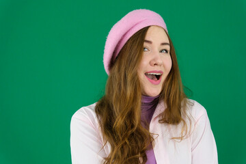 young girl woman with a pink beret on her head France fashion on a green background chromakey. different emotions pink jacket gloves long brown hair. pink winter autumn knitted gloves on hands
