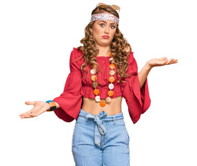 Young blonde girl wearing bohemian and hippie style clueless and confused expression with arms and...