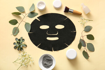 Facial sheet mask with different cosmetic products, gypsophila flowers and leaves on yellow...