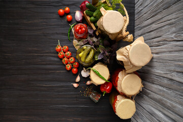 Canned cherry tomatoes and cucumbers in jars on a wooden background, top view