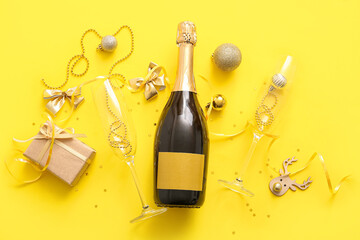 Bottle of champagne with glasses,  Christmas decorations and gift box on yellow background