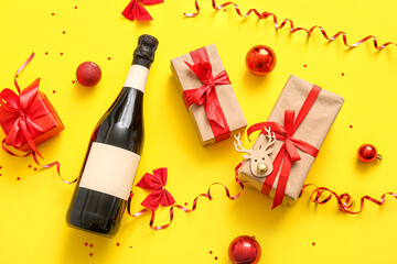 Bottle of champagne with Christmas balls and gift boxes on yellow background