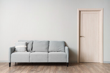 Grey sofa with cushion near light wall in room