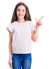 Cute hispanic child girl wearing casual white tshirt with a big smile on face, pointing with hand finger to the side looking at the camera.