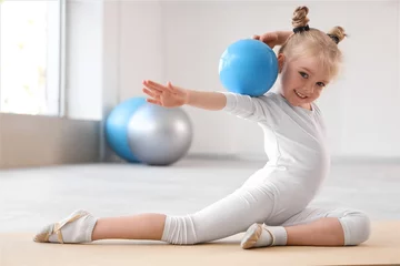 Fotobehang Cute little girl doing gymnastics with ball on mat in gym © Pixel-Shot