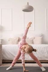 Poster Cute little girl doing gymnastics on mat in bedroom © Pixel-Shot