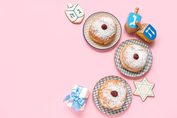 Plates with donuts, gift and dreidels for Hanukkah celebration on pink background