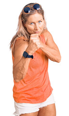 Middle age fit blonde woman wearing casual summer clothes and sunglasses ready to fight with fist...