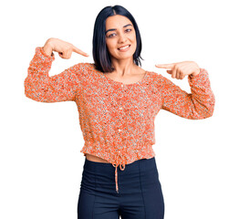 Young beautiful latin woman wearing casual clothes looking confident with smile on face, pointing...