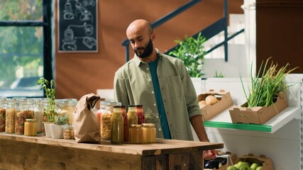 Eco conscious man buying fresh food in a local grocery store with homegrown produce, looking for chemicals and additives free products. Middle eastern person examining shelves with spices.