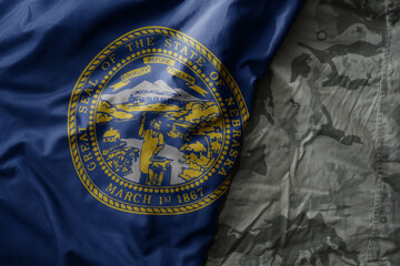 waving flag of nebraska state on the old khaki texture background. military concept.