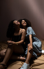 Portrait of two young and beautiful friends sitting, looking up smiling. Studio low light.