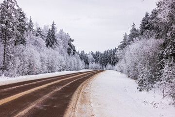 Obraz premium Picturesque winter view of highway with snow-draped forest trees on cloudy, frosty day. Sweden.