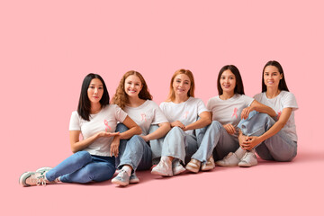 Beautiful women with pink ribbons sitting on color background. Breast cancer awareness concept