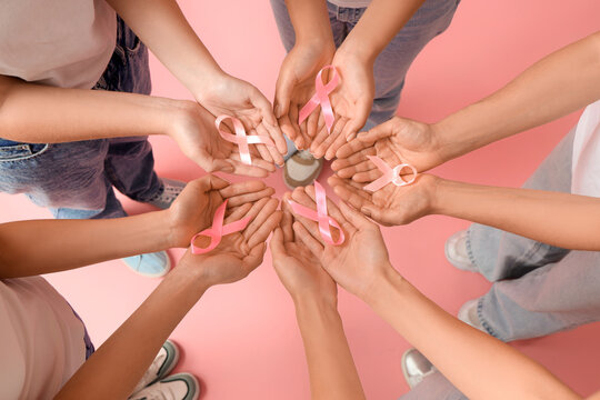 Women with pink ribbons on color background, top view. Breast cancer awareness concept