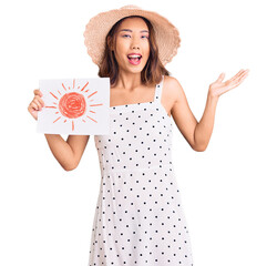 Young beautiful chinese girl wearing summer hat holding sun draw celebrating victory with happy...