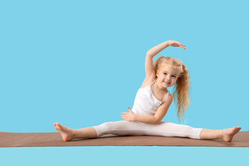 Cute little happy girl doing gymnastics on mat against blue background