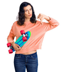 Young beautiful hispanic woman holding skate with angry face, negative sign showing dislike with thumbs down, rejection concept © Krakenimages.com