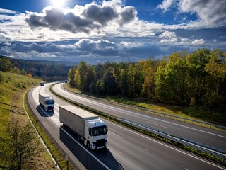 Three white trucks driving on the highway winding through forested landscape in autumn colors at...