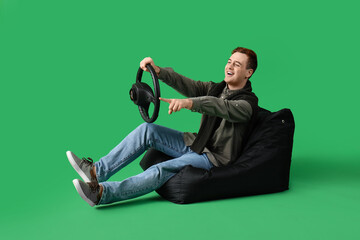 Young man with steering wheel pointing at something on green background