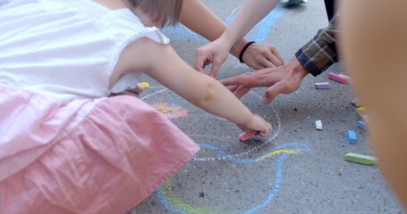 Kids and adult hands close up. Drawings details on the asphalt as result of play and fun. Children and adults use chalk to create temporary and colorful pictures outdoors. Interactive street art - obrazy, fototapety, plakaty