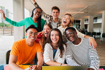 Group of young teenage students siting at library, using a laptop and looking at camera. Happy classmates studying and doing homeworks at high school. Multiracial academy people portrait. Schoolboys