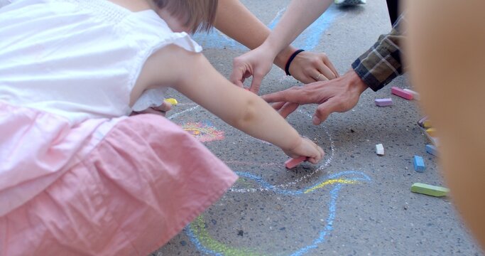 Kids and adult hands close up. Drawings details on the asphalt as result of play and fun. Children and adults use chalk to create temporary and colorful pictures outdoors. Interactive street art