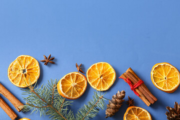Dried orange slices with fir branches, cinnamon, star anise and pine cone on blue background