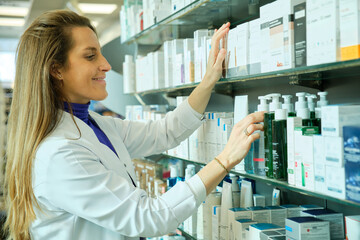 Young pharmacist smiling placing products on the shelf in a pharmacy
