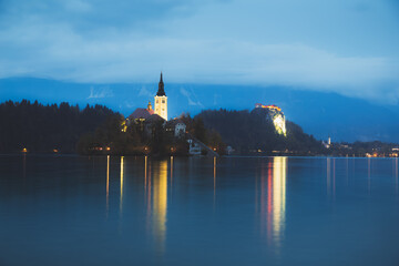 Evening twilight view of Pilgrimage Church of the Assumption of Maria Bled Castle lit up at Lake...