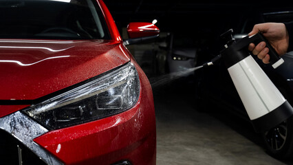 A man washes the headlights of a red car with a spray. 