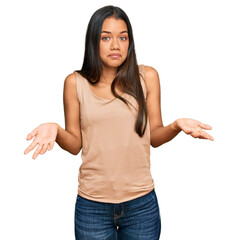 Beautiful hispanic woman wearing casual clothes clueless and confused expression with arms and...