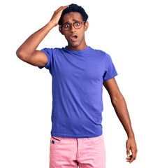 Fototapeta premium African handsome man wearing casual clothes and glasses surprised with hand on head for mistake, remember error. forgot, bad memory concept.